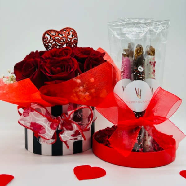 Red roses in a striped box beside chocolate-covered pretzel sticks