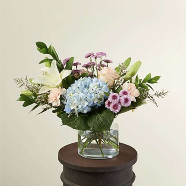 Mixed bouquet with blue hydrangea, lilies, and pink flowers in a glass vase
