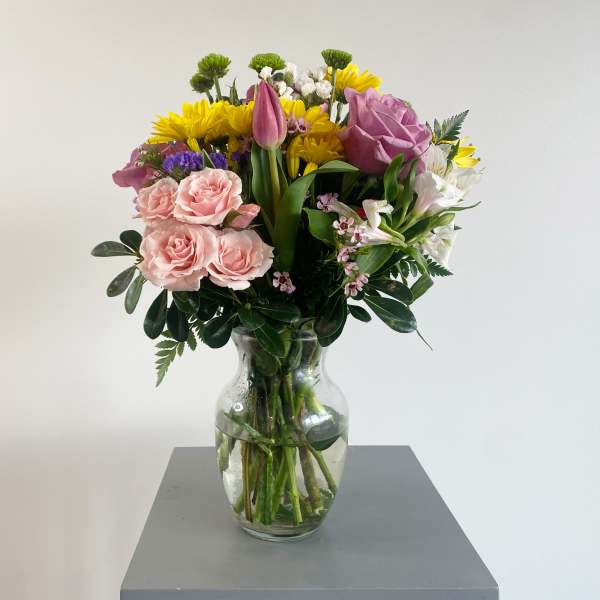 Mixed bouquet of pink roses, yellow daisies, and white flowers in a glass vase