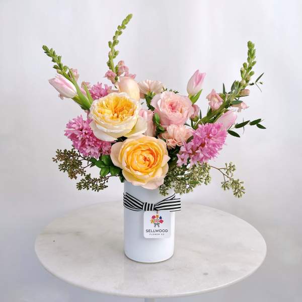 Pink and yellow roses with snapdragons in a white vase