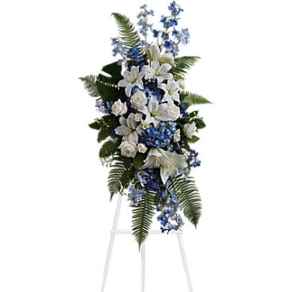 Standing floral spray with white lilies and blue flowers on an easel
