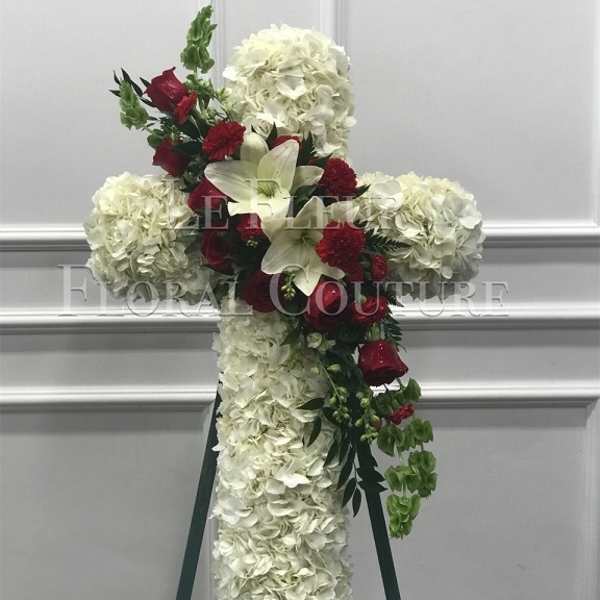 White floral cross on an easel with red roses and lilies