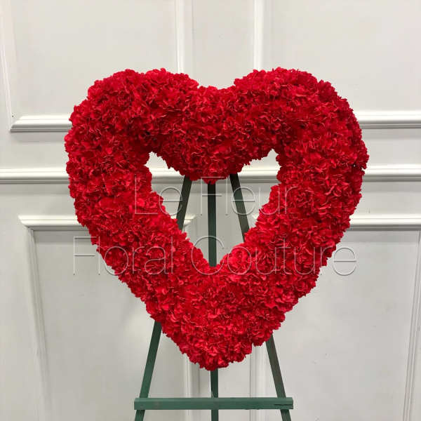 Red carnation heart-shaped standing floral wreath on an easel