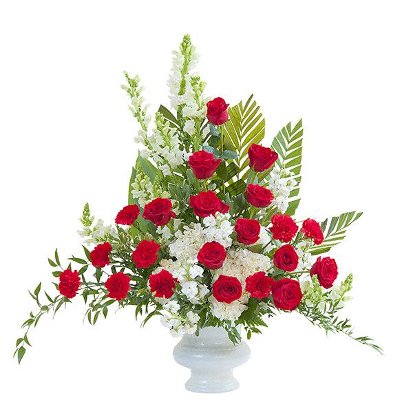 Tall red and white flower arrangement with roses and carnations in a white pedestal vase