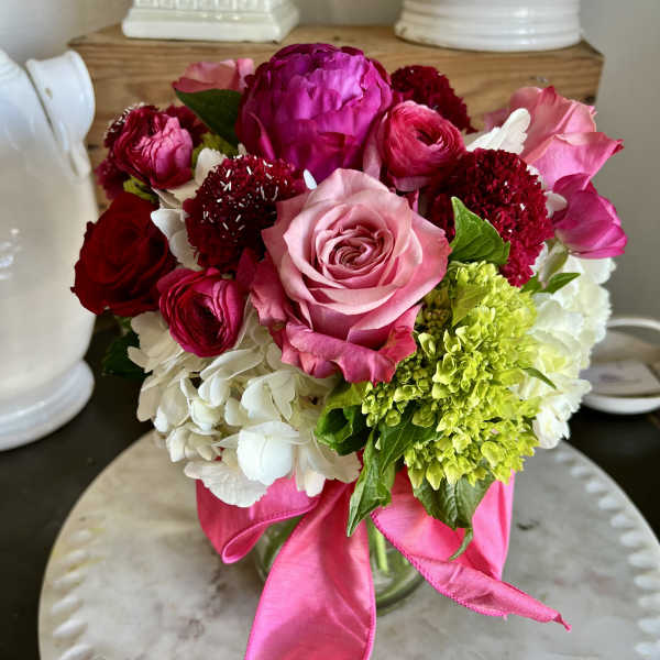 Pink and red mixed flower bouquet in a glass vase with a ribbon