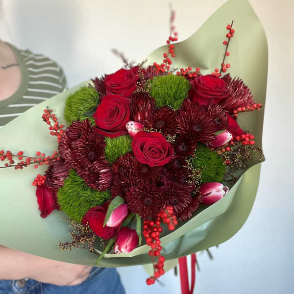 Bouquet of red roses and burgundy flowers wrapped in pale green paper