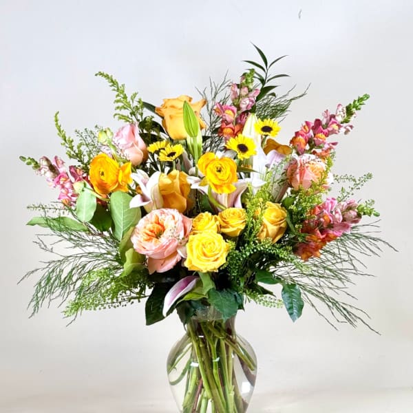 Tall mixed bouquet of yellow and peach roses, lilies, daisies, and snapdragons in a clear glass vase