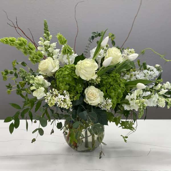 White roses and snapdragons in a glass vase with green hydrangea