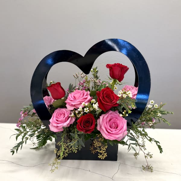 Heart-shaped floral arrangement with pink and red roses in a black box