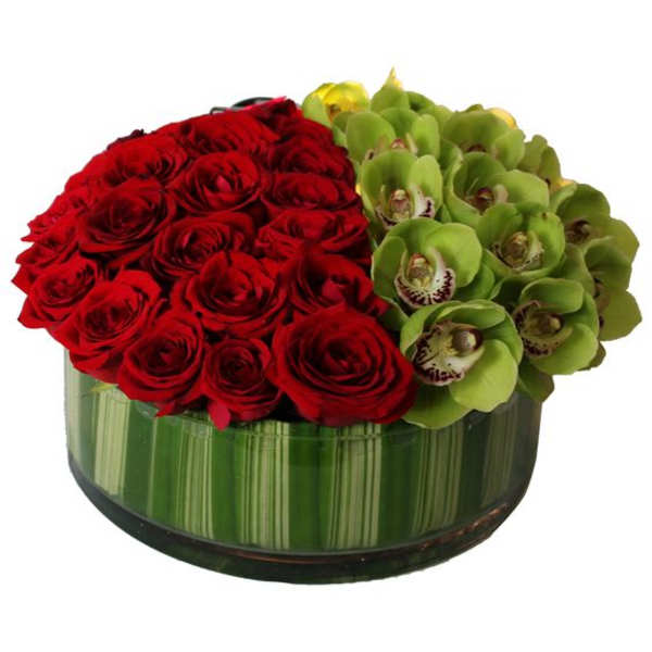 Red roses and green orchids arranged in a round glass vase