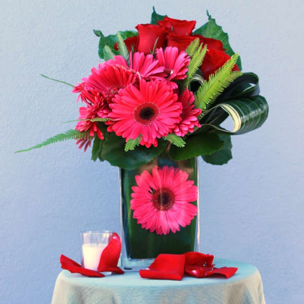 Pink gerbera daisies and red roses in a tall glass vase