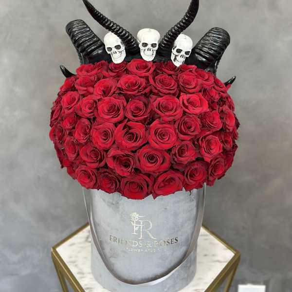 Red roses arranged in a gray hat box with black horn decorations and skull toppers