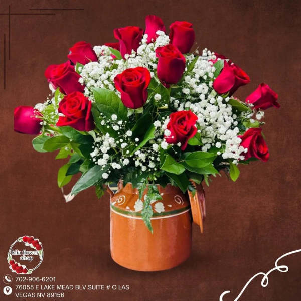 Red rose bouquet with white filler flowers arranged in an orange ceramic pitcher.