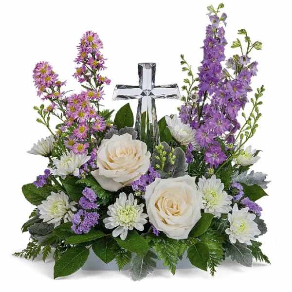 White roses and purple flowers arranged around a clear glass cross