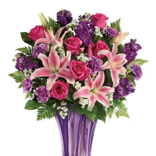 Pink lilies, roses, and purple flowers arranged in a tall purple glass vase