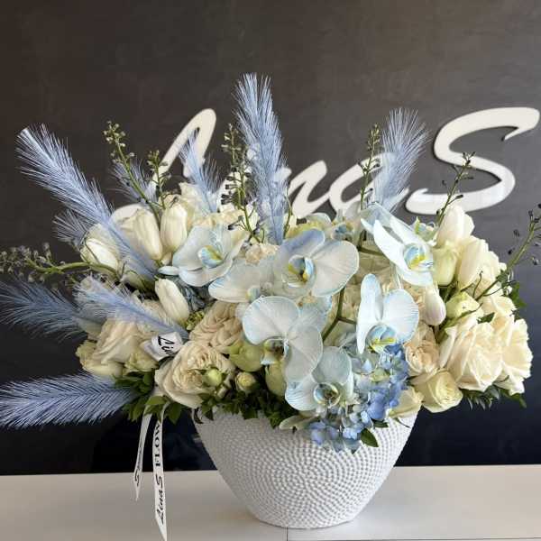 White floral arrangement with pale blue orchids in a textured white vase