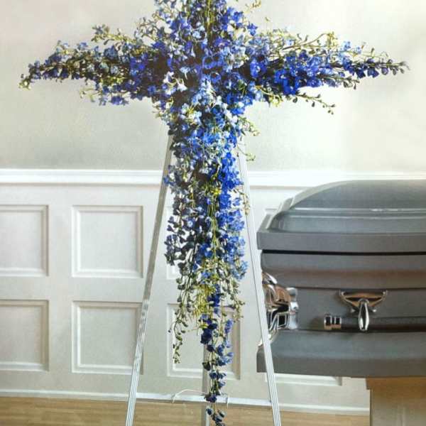Blue floral cross on a stand beside a casket