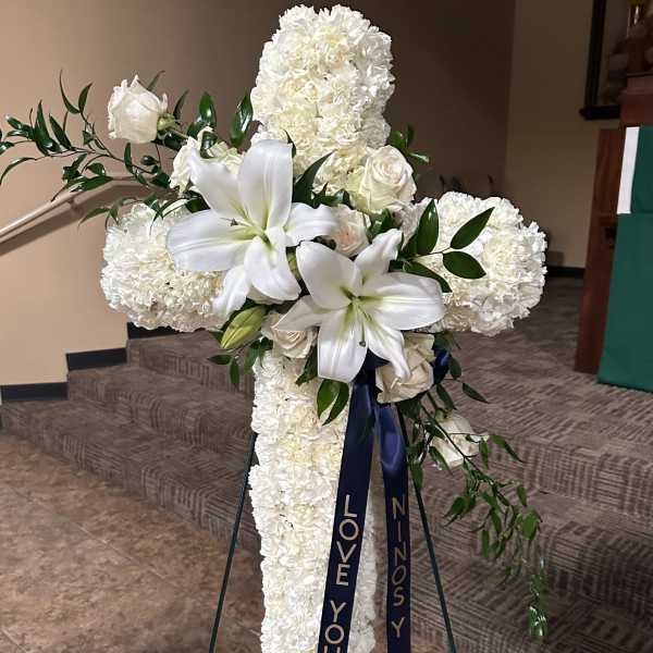 White floral cross on a stand with ribbon streamers