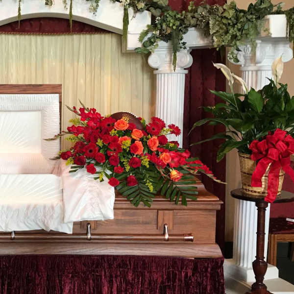 Casket spray with red and orange flowers beside matching potted plants