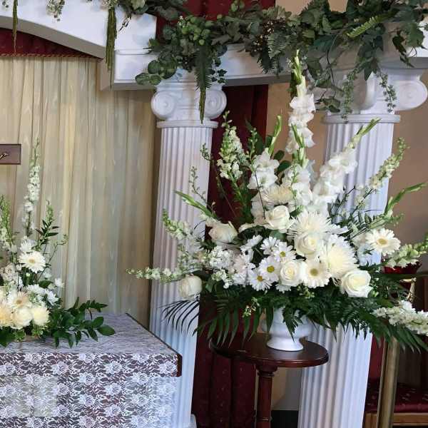 White floral funeral altar with tall arrangements and a crucifix