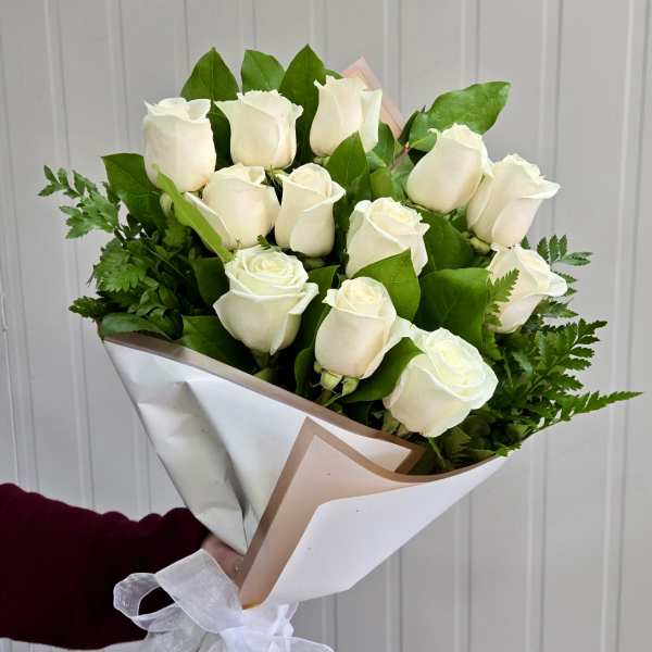 Bouquet of white roses wrapped in white paper with green foliage