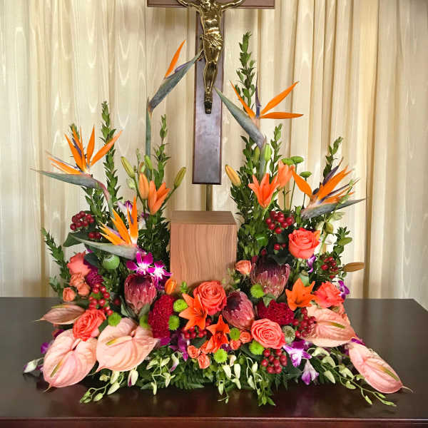 Large floral arrangement with orange birds of paradise and roses beneath a crucifix