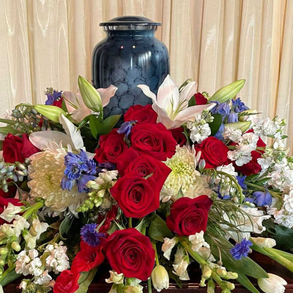 Large floral arrangement with red roses, white lilies, and blue flowers in a blue vase