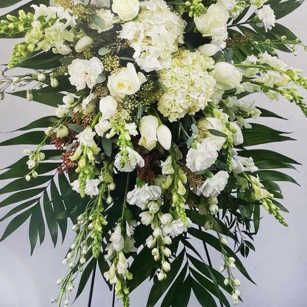 Large white floral standing spray with cascading blooms and dark palm leaves