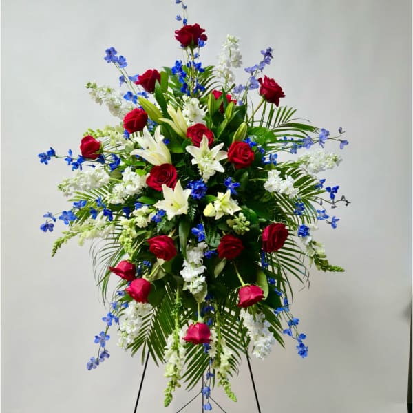 Standing floral spray with red roses, white lilies, and blue flowers