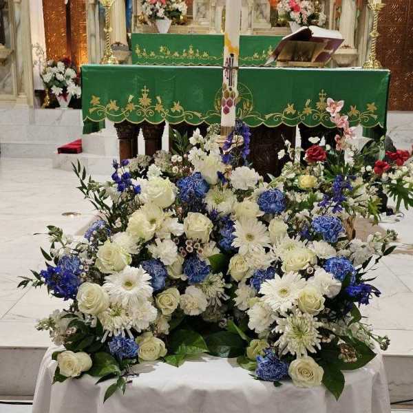Low blue and white altar arrangement with roses and mums around a tall decorative candle