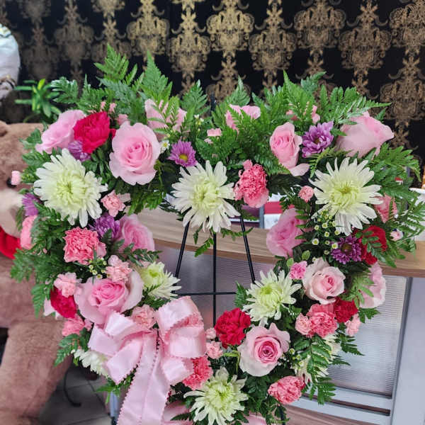 Heart-shaped floral wreath on a stand with pink and white flowers