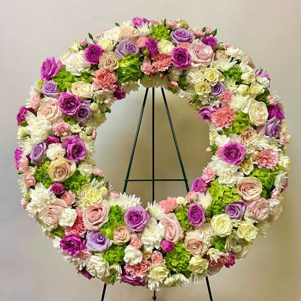 Large circular floral wreath with pink, purple, white, and green blooms on a stand