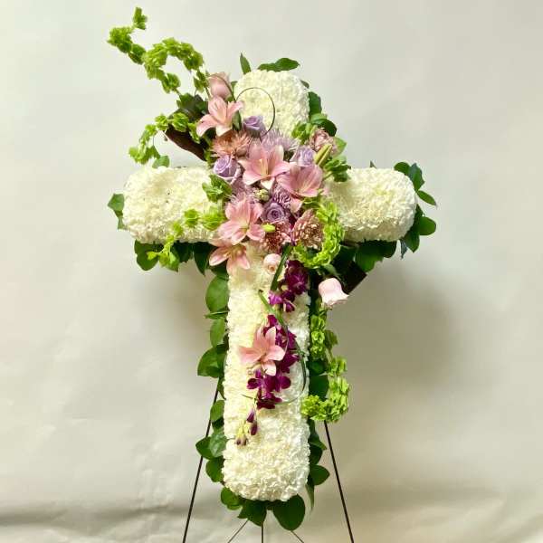 White floral cross on an easel with pink and purple flowers
