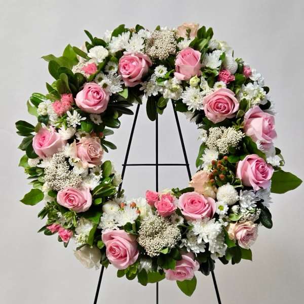 Pink roses and white flowers arranged in a circular wreath on a stand