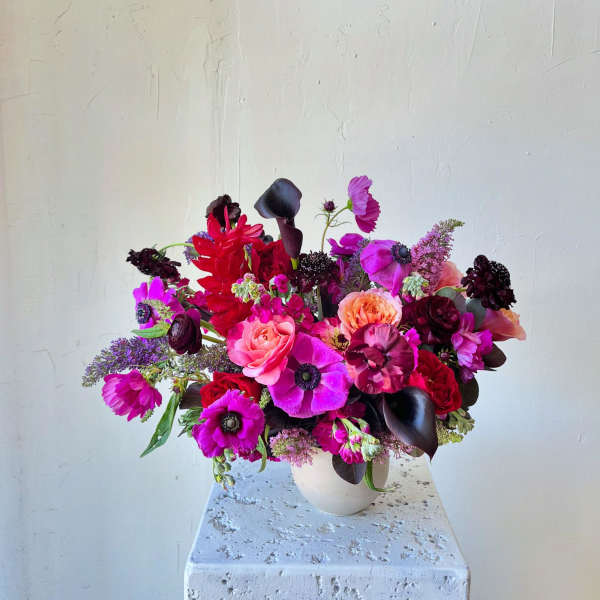 Bright mixed bouquet in a white vase with pink, red, purple, and peach blooms