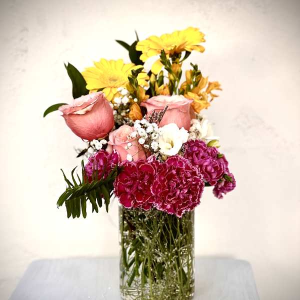 Mixed bouquet of pink roses, yellow daisies, and magenta carnations in a clear glass vase