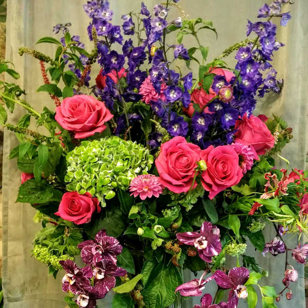 Tall bouquet of pink roses, purple flowers, and orchids in a glass vase