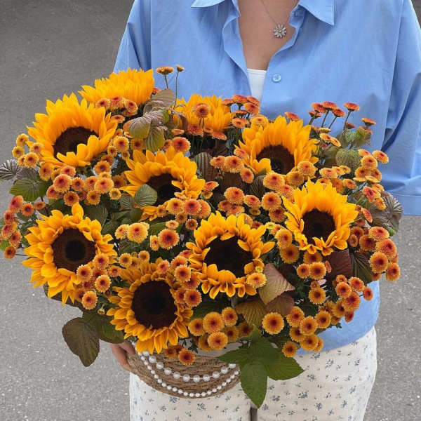 Large bouquet of sunflowers and small orange mums in a woven basket