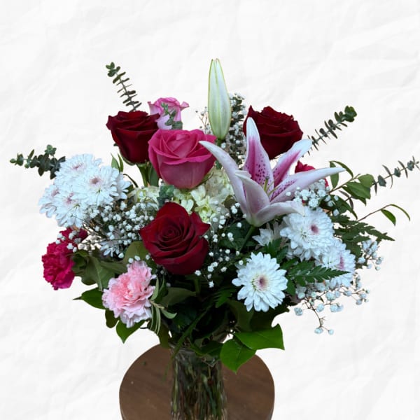 Mixed bouquet of roses, lilies, and daisies in a glass vase