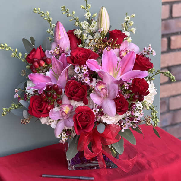 Bouquet of red roses and pink lilies in a glass vase with a ribbon
