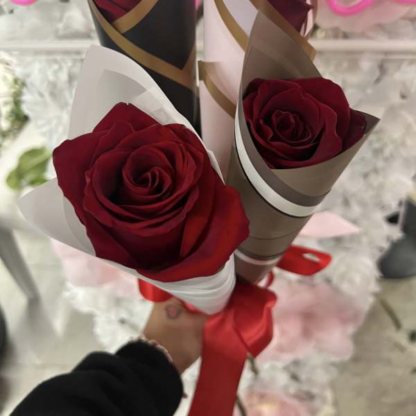 Three red roses wrapped in decorative paper with a red ribbon