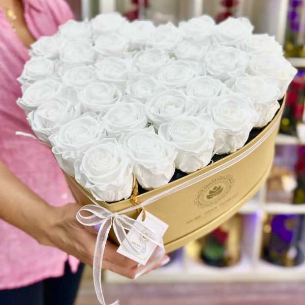 Heart-shaped gold box filled with white roses held by a person in a shop