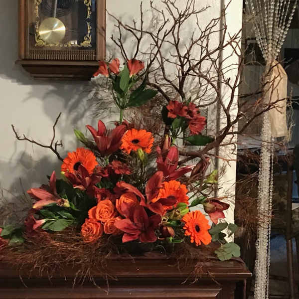 Orange and red floral arrangement with branches in a low container