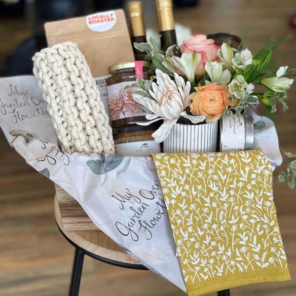 Gift basket with flowers, wine bottles, candles, and a knitted item