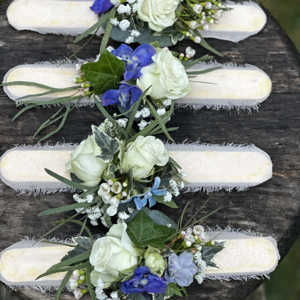 Four floral wrist corsages with white roses and blue flowers on pale bands