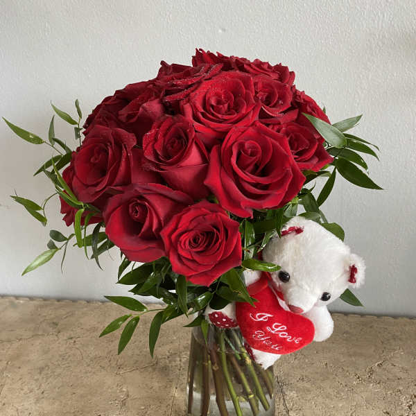 Red roses in a glass vase with a small white teddy bear