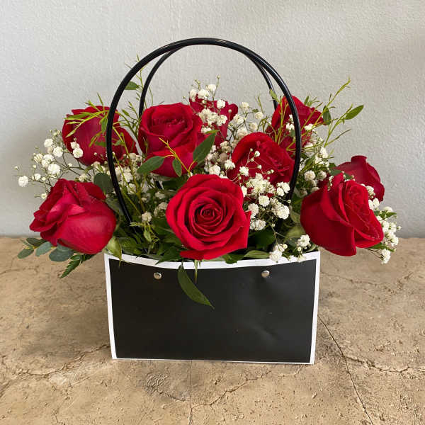 Red roses in a black handled gift bag with white baby's breath
