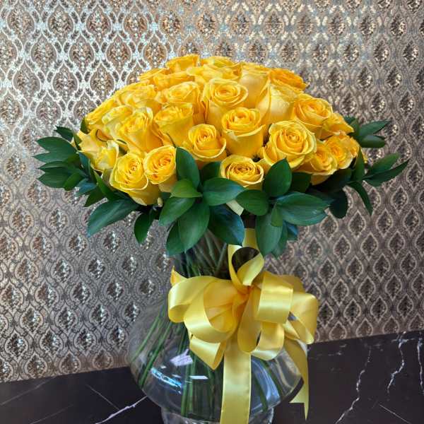 Yellow rose bouquet in a clear glass vase with a yellow ribbon