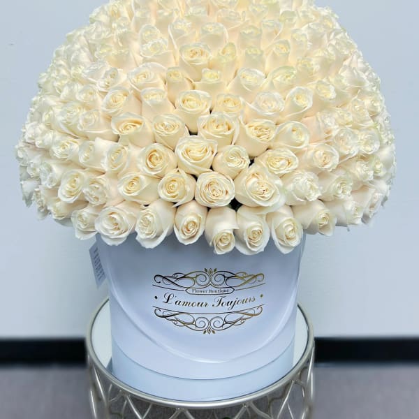 Large dome of cream roses arranged in a white hat box on a small table