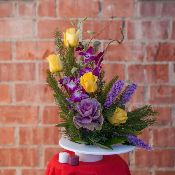 Purple and yellow floral arrangement on a white pedestal stand